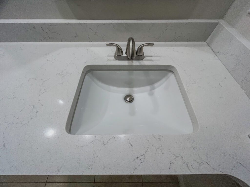 Close-up of remodeled bathroom sink with a white quartz countertop and sleek chrome faucet, installed by skilled bathroom remodeling contractors in Southwest Florida. | Sun Control Aluminum & Remodeling