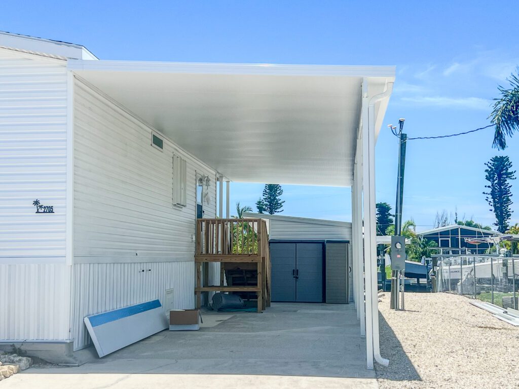 Side view of a mobile home with a newly installed aluminum-covered carport featuring hurricane shutters and durable materials, completed by experienced carport installers in Southwest Florida | Sun Control Aluminum & Remodeling